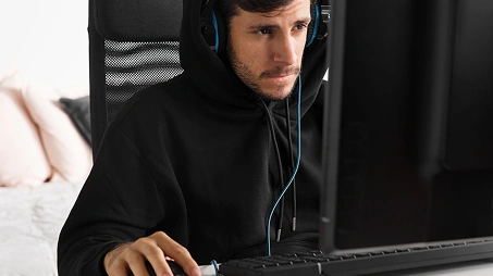 Een fanatieke gamer met een koptelefoon op, die 's avonds laat achter het scherm speelt in een geoptimaliseerde gaming-setup.