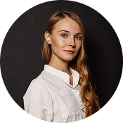 Professioneel portret van een jonge vrouw met lang blond haar, gekleed in een witte blouse, tegen een donkere studioachtergrond.